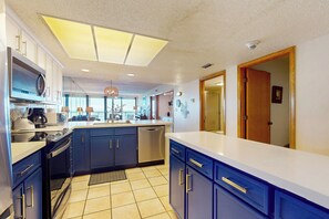 Una cocina moderna con armarios azul oscuro, encimera blanca y una isla grande. Hay un lavavajillas, una estufa y un fregadero.