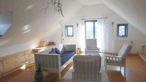 Ein geräumiges Dachzimmer mit schrägen Wänden, einem Bett, einem Sessel und einem kleinen Tisch.