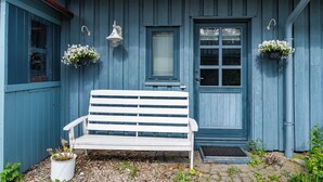 Eine weiße Bank vor einem blauen Holzhaus mit Tür und Fenstern.
