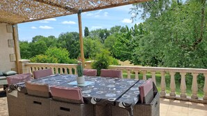 Een terras buiten met een tafel en stoelen, omringd door een houten pergola en een stenen balustrade.