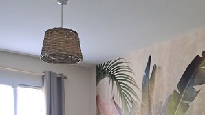 Een slaapkamer met een bed, nachtkastje, lamp, muurschildering en een raam met gordijnen.