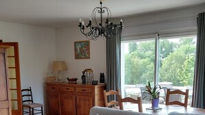 Een woonkamer met een bank, een houten kast, een kroonluchter en uitzicht op groen.