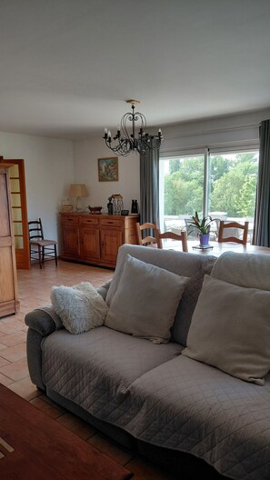 Ein Wohnzimmer mit Sofa, Holzschrank, einer Kristallleuchtre und Blick auf Grünflächen.