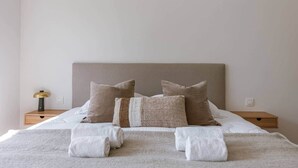 A neatly made bed with a beige headboard, two bedside tables with lamps, and a wall switch. - Brand new house Sable d'Or  - Oostduinkerke (Koksijde)