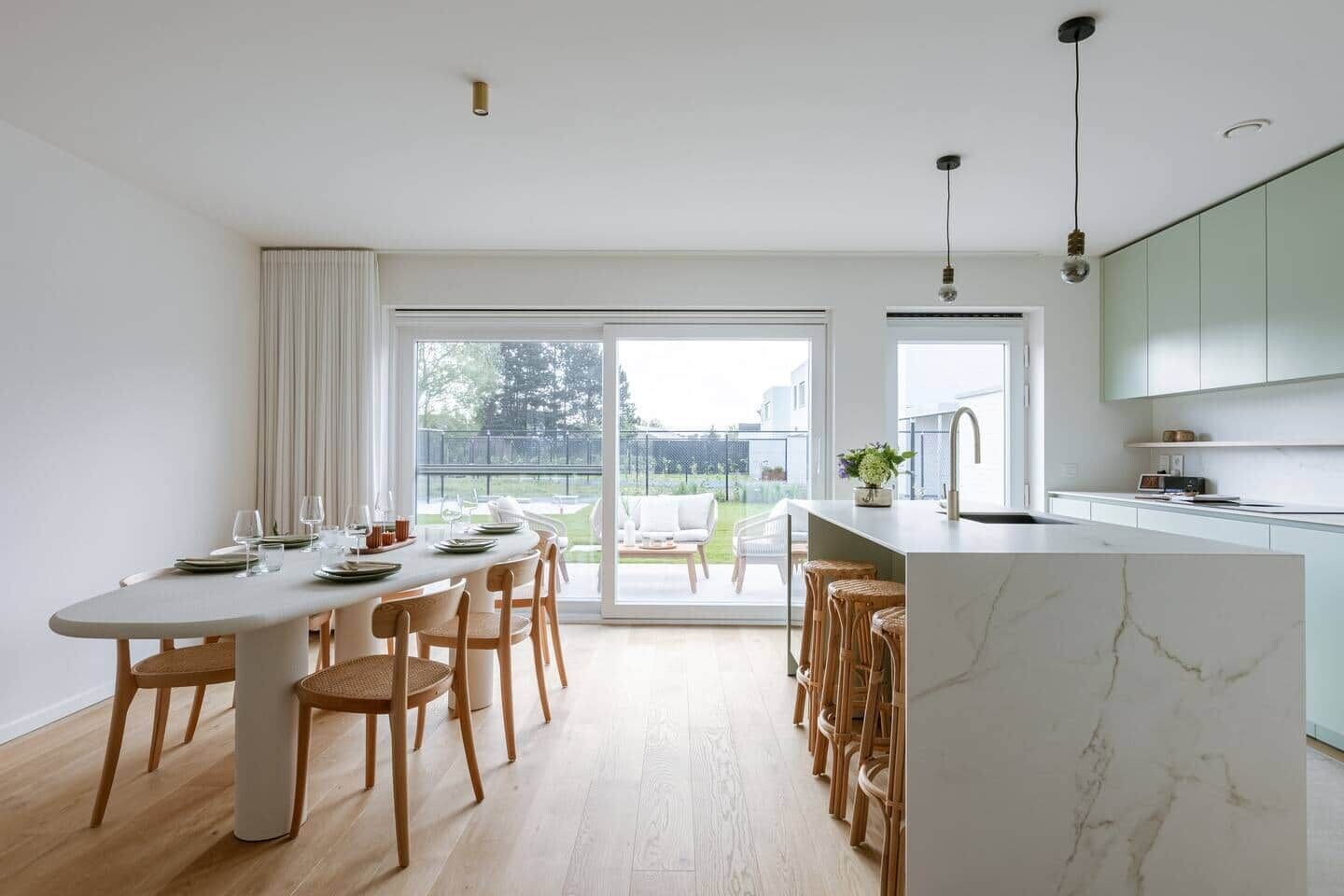 Una cucina moderna con isola in marmo, sedie in legno e zona pranzo con una porta vetrata che dà su un patio.