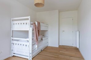 Ein Zimmer mit einem weißen Etagenbett, einer Tür und Holzdielen.