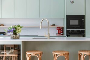 Una cocina moderna con un grifo de acero inoxidable, un microondas empotrado y una cafetera roja sobre la encimera.