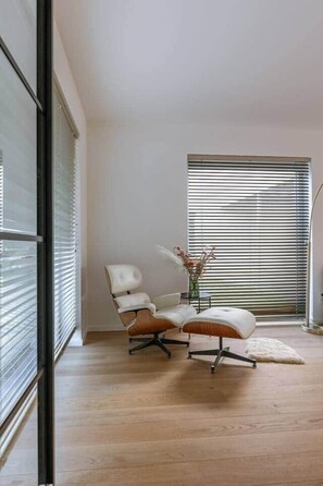 A modern room with a large window, a white chair, a small table with a vase, and a fluffy rug. - Brand new house Sable d'Or  - Oostduinkerke (Koksijde)