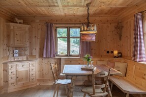 A wooden cabin interior with a dining table, chairs, a bench, a window with curtains, and a cabinet. - Luxury Detached Panoramic Mountain Home (Tschagguns)