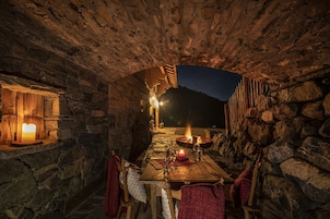 Comedor con paredes de piedra, una mesa dispuesta para dos, una vela y un hogar.