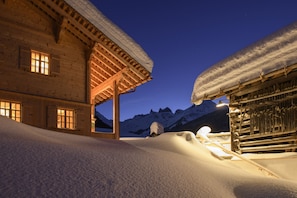 A wooden chalet with a snow-covered roof, a wooden staircase, and a mountain backdrop. - Panorama Deluxe Mountain Hideaway House (Tschagguns)