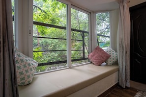 A window seat with cushions, a view of trees, and a door. - Deodar Bungalow & Cottage by Trikone (Nainital)