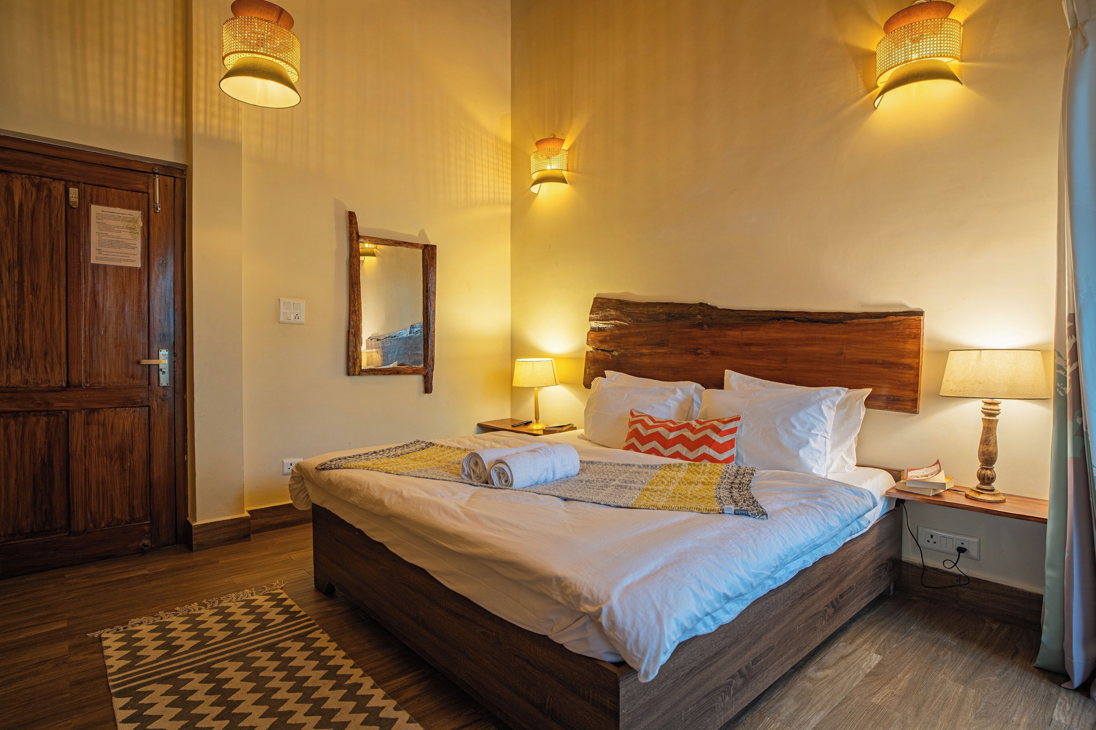 A neatly made bed with a wooden headboard, a bedside table with a lamp, and a patterned rug on the floor.