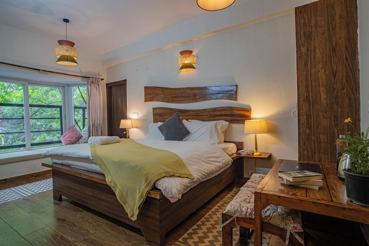 Une chambre à coucher avec un lit en bois, des lampes de chevet, une fenêtre donnant sur un beau paysage et une table de chevet en bois agrémentée d’une plante.
