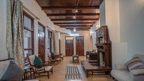 A spacious living room with wooden furniture, a fireplace, and a view of the outside. - Deodar Bungalow & Cottage by Trikone (Nainital)