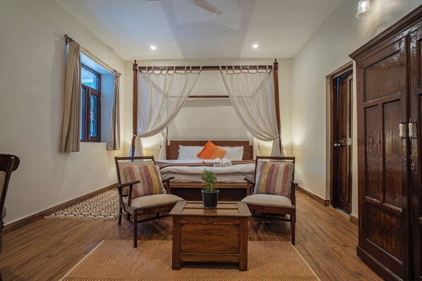 Quarto com cama de dossel, duas poltronas, mesa de centro de madeira e um guarda-roupa grande.