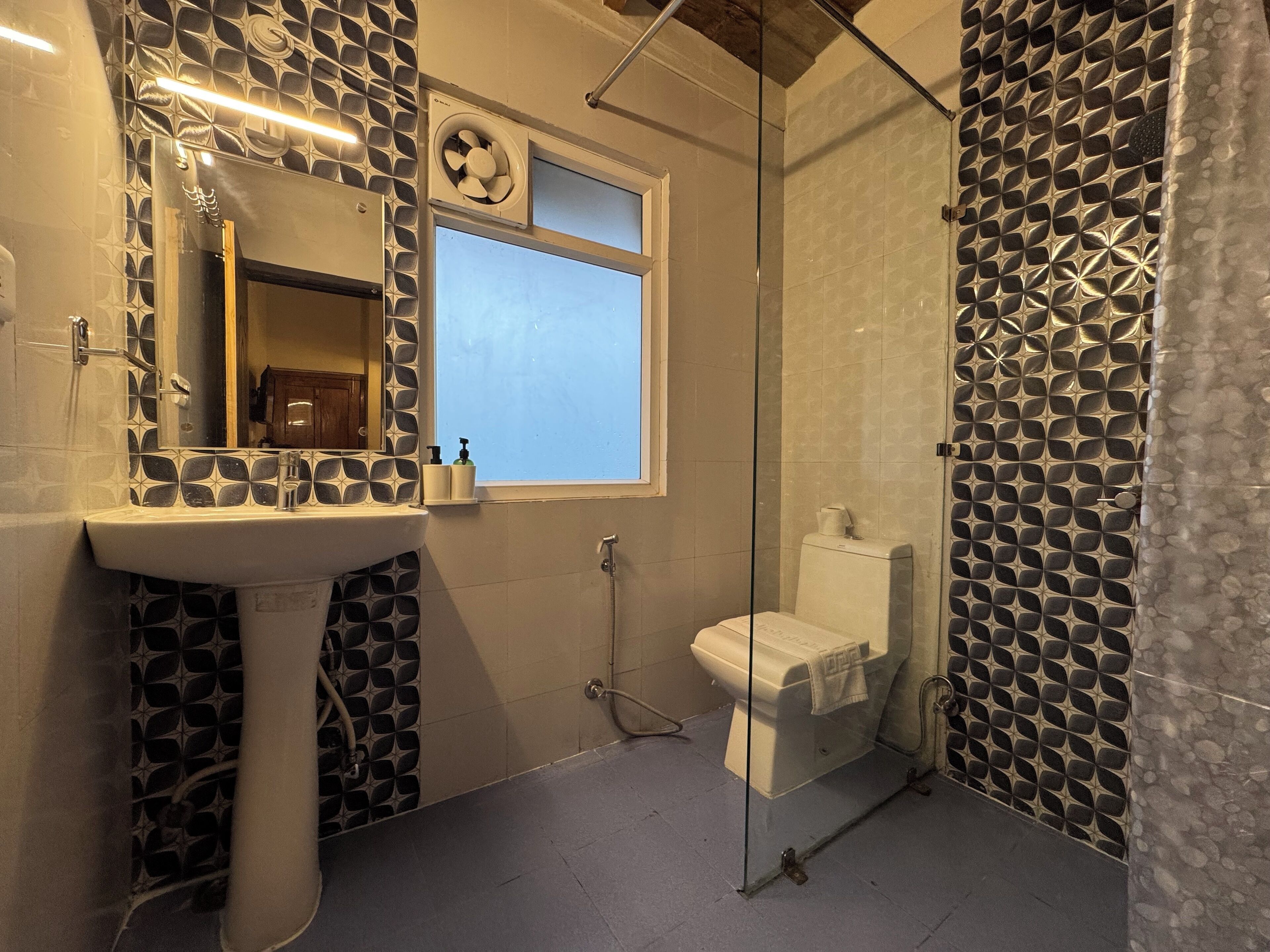 A bathroom with a sink, mirror, window, toilet, and shower area.