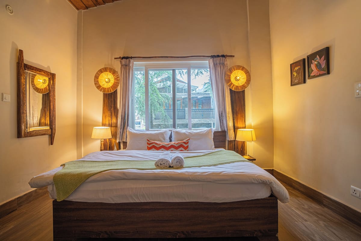 Un lit bien fait, recouvert d’une couverture verte, avec deux lampes de chevet et une fenêtre avec des rideaux.