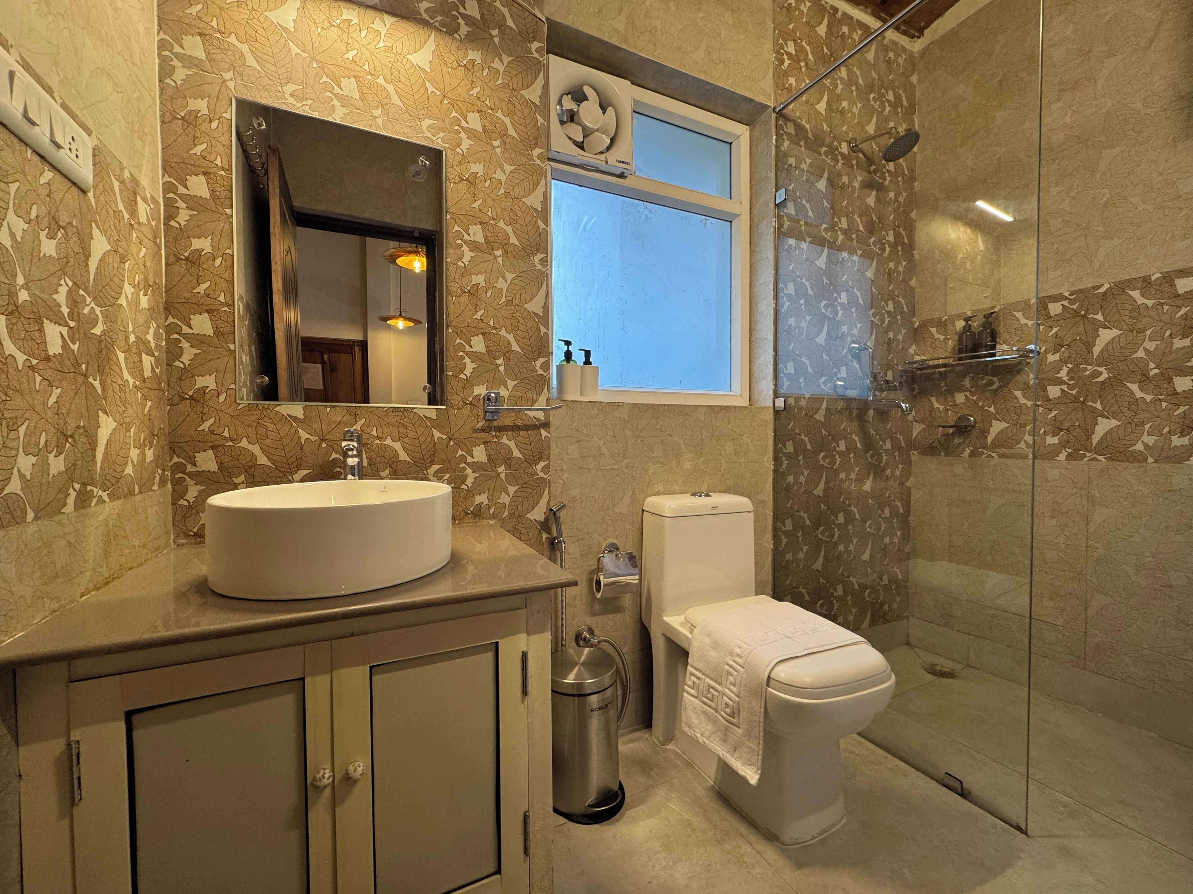 A bathroom with a round sink, toilet, and a glass shower enclosure.