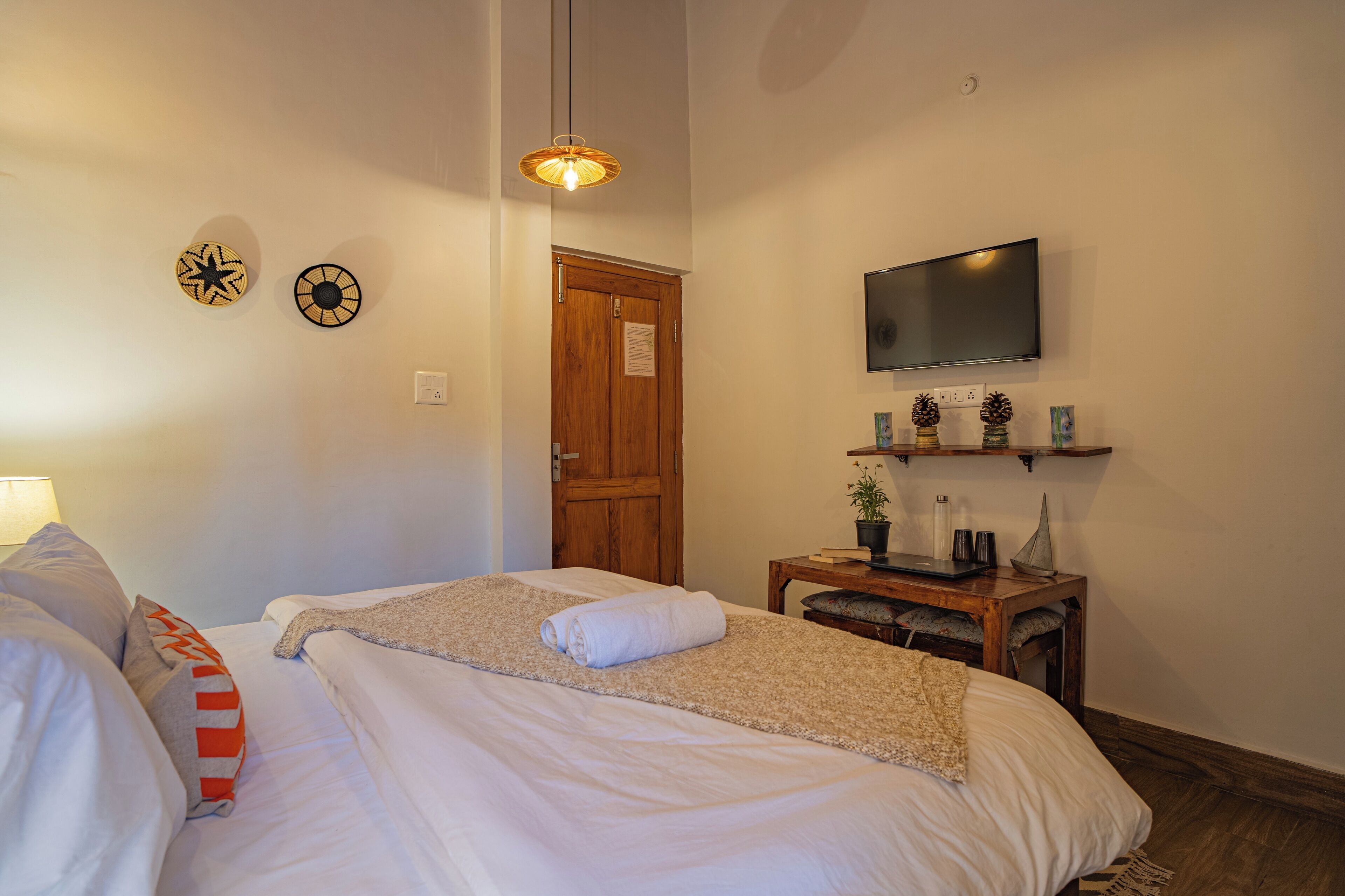 A bedroom with a bed, a television, a wooden door, and a small table with a plant and decorative items.