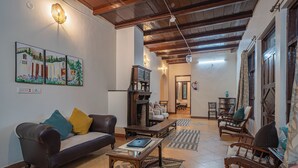 A living room with a sofa, coffee table, and wooden chairs. There is a fireplace, a dining area, and artwork on the wall. - Deodar Bungalow & Cottage by Trikone (Nainital)