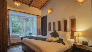 A bedroom with a large bed, a bedside table with a lamp, a window with curtains, and a view of greenery outside. - Deodar Bungalow & Cottage by Trikone (Nainital)