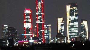 Une vue nocturne sur les gratte-ciel d’une ville, avec les bâtiments illuminés qui se reflètent dans l’eau.