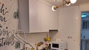 Une cuisine de taille réduite avec des meubles blancs, un évier en acier inoxydable, un four à micro-ondes et un luminaire décoratif.