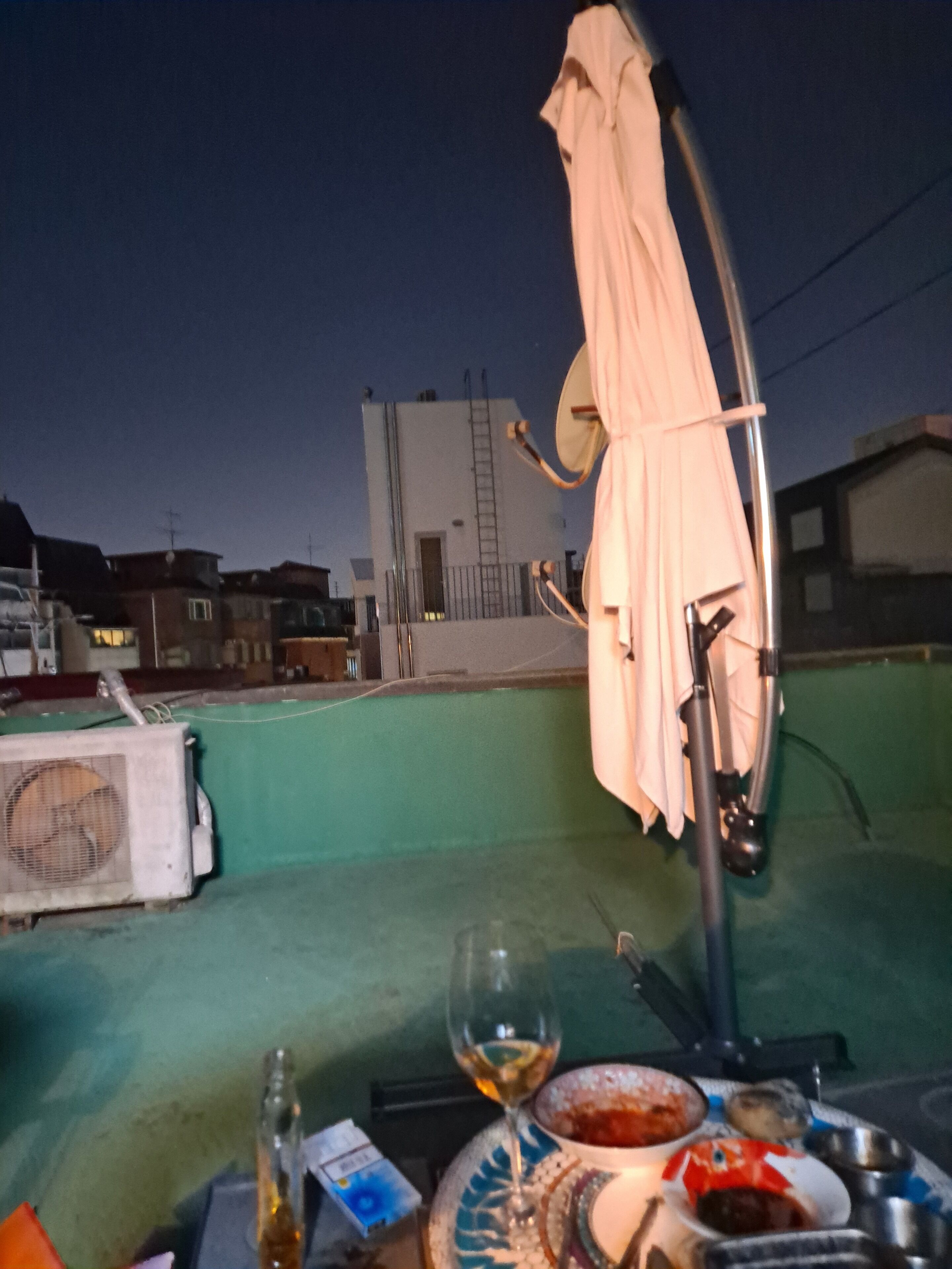 A rooftop terrace with a table set for dining, a satellite dish, and a view of buildings in the background.