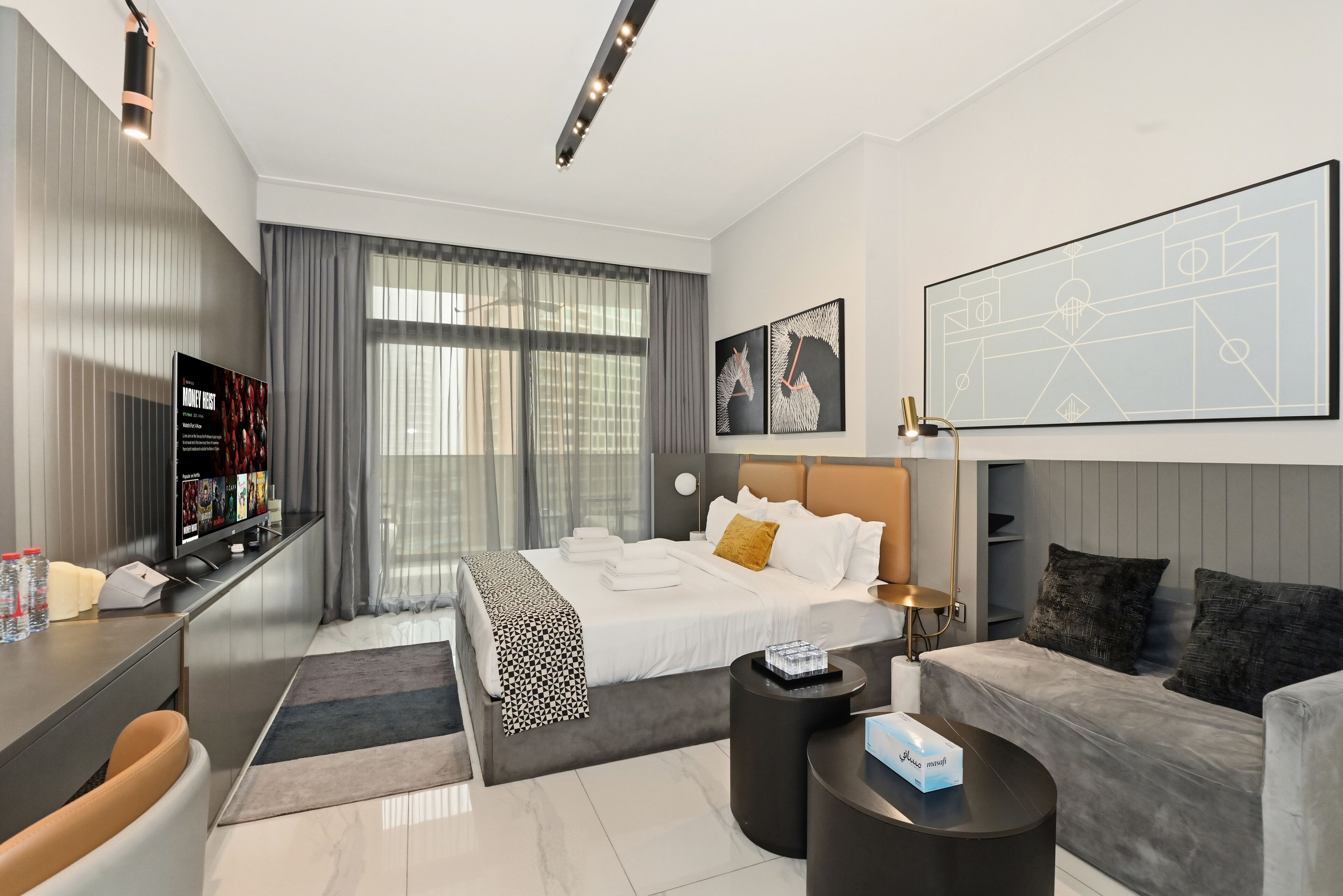 A modern hotel room with a neatly made bed, a sofa, a coffee table, and a TV on a stand.