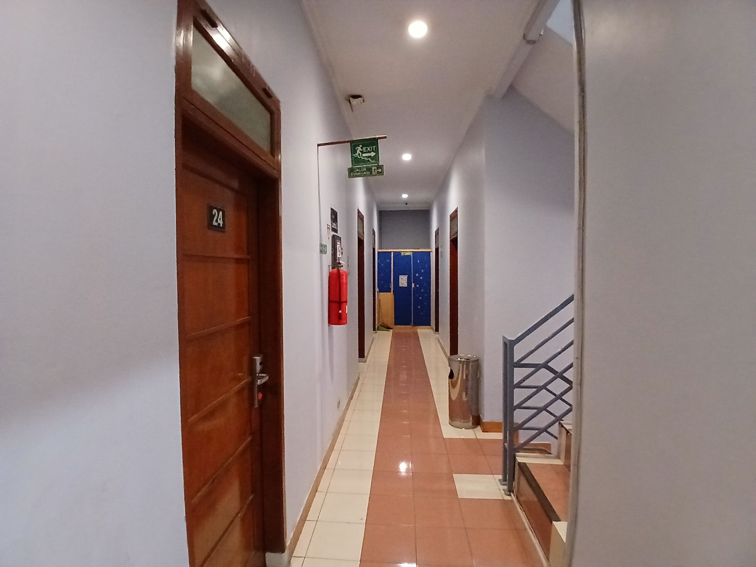Un pasillo con un extintor, una puerta azul y una escalera.