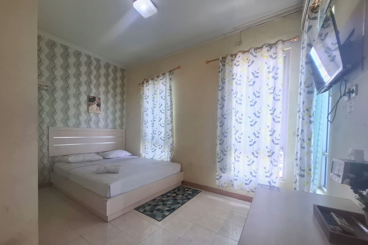 A bedroom with a bed, curtains, a TV, and a small table with a plant.