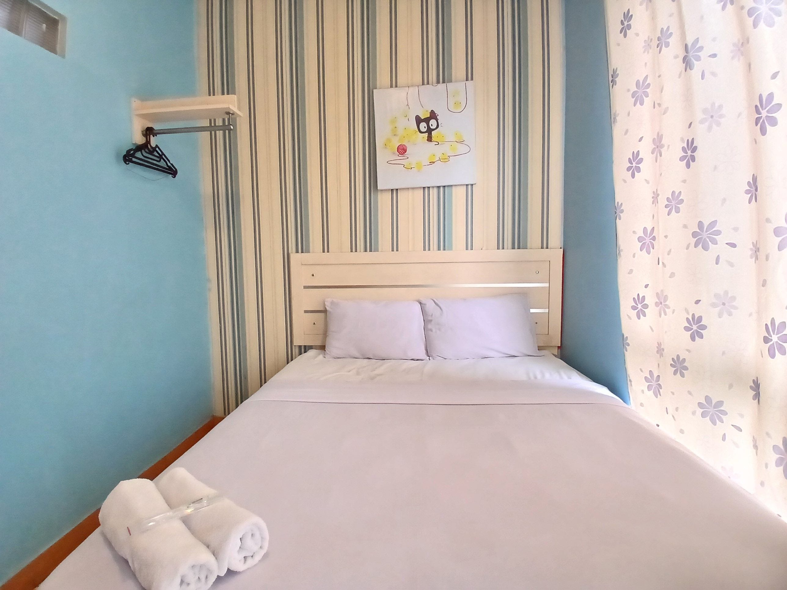A neatly made bed with white linens, a headboard, and a wall-mounted towel rack.