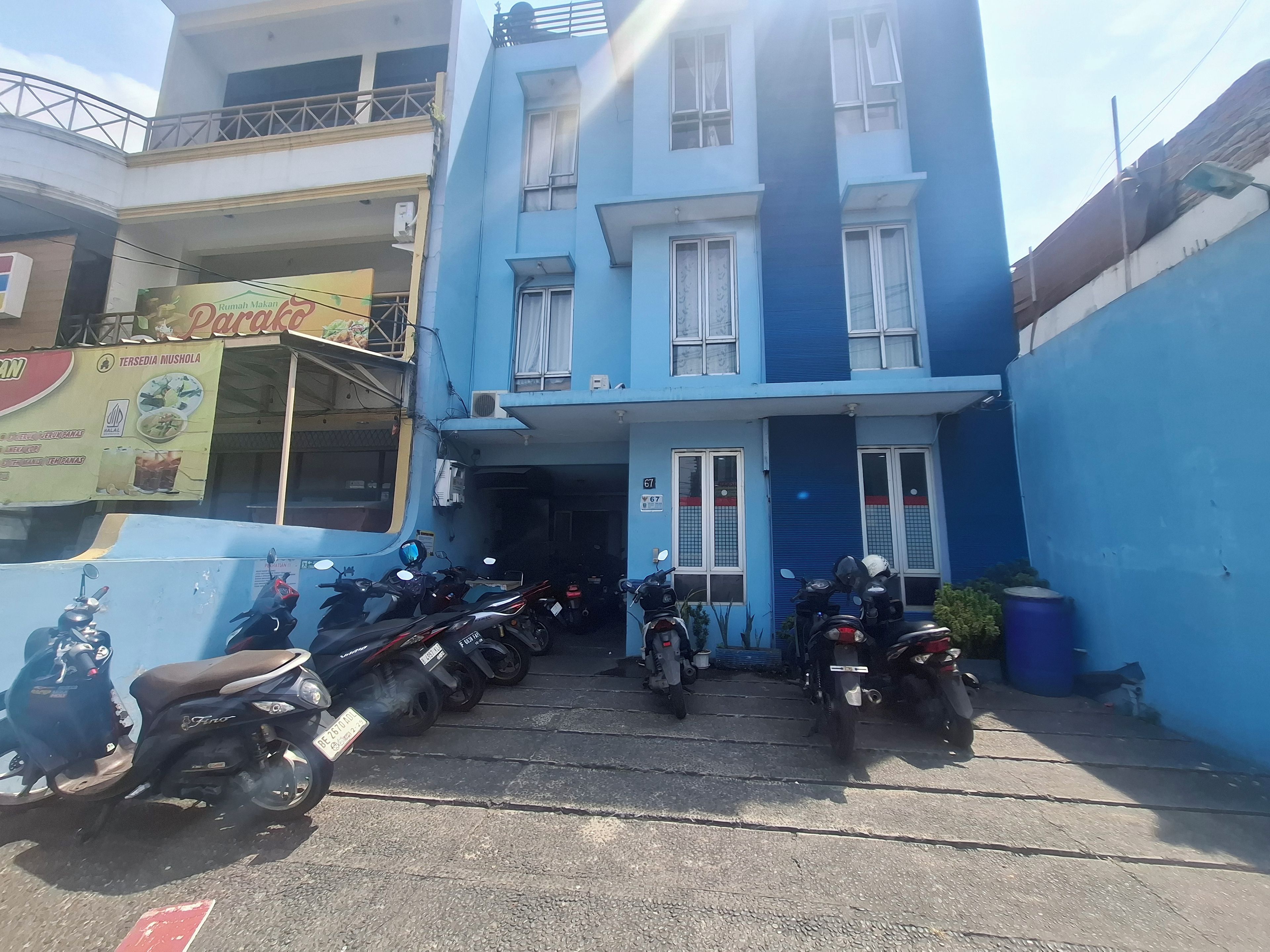 Un edificio a più piani con facciata blu, ingresso coperto e una fila di motociclette parcheggiate.
