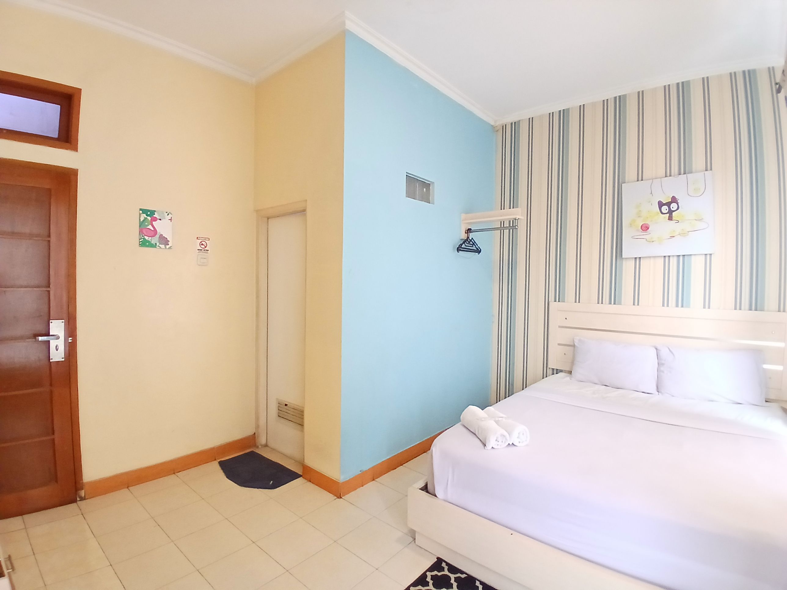 Ein Hotelzimmer mit Bett, Tür, Wand mit Streifenmuster und einem kleinen Fenster.