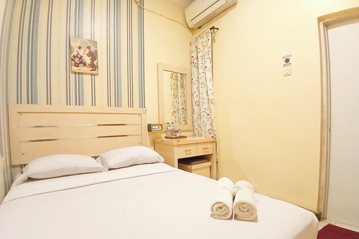 Una habitación de hotel con una cama, una mesita de noche, un espejo y una ventana con cortinas.