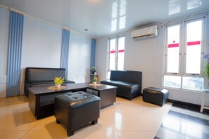 Habitación de hotel moderna con cama, sofá, mesita de centro y una pequeña mesa con una planta.