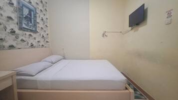 Ein schlichter, kleiner Raum mit einem Bett, einem Schreibtisch und einem an der Wand befestigten Fernseher.