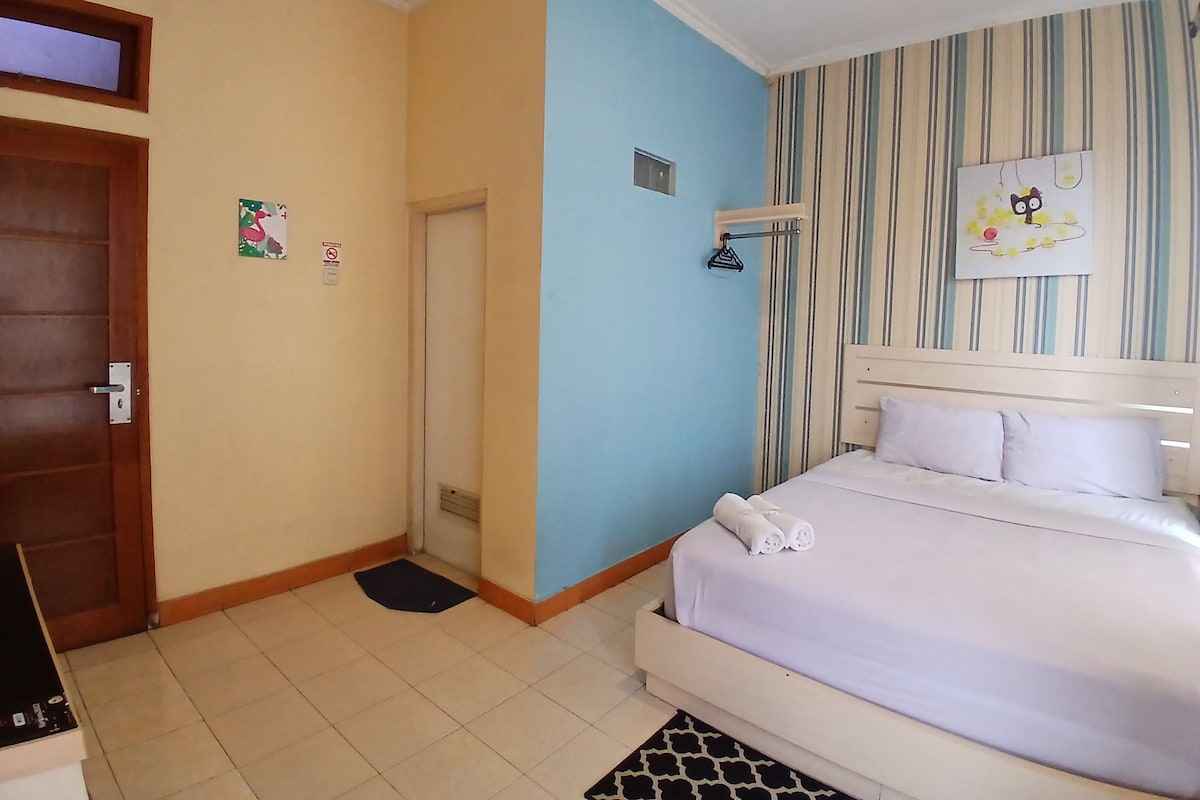 Habitación de hotel con cama, puerta, pared con diseño a rayas y una ventana pequeña.