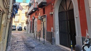 Una stretta strada acciottolata fiancheggiata da edifici con balconi e condizionatori, con uno scooter parcheggiato sul lato.
