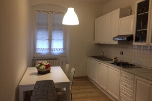 A compact kitchen with white cabinets, a white countertop, a dining table with chairs, and a hanging pendant light. - The house is located in the centre of La Spezia, close to Central Station: a strategical and convenient position to visit the city and to reach all places of Cinque Terre by train. The apartment consists of a large double bedroom, bright and cosy living  (La Spezia)