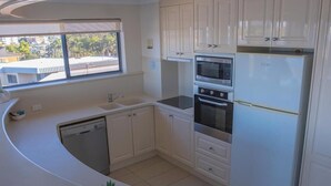 Een compacte keuken met witte kastjes, een vaatwasser, een oven en een koelkast.