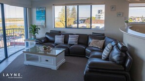 Een woonkamer met een leren bank, een glazen salontafel en uitzicht op het groen door grote ramen.