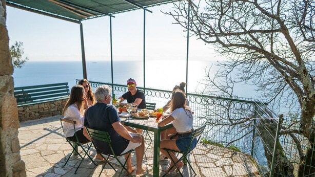 Un grupo de personas cenando en una mesa al aire libre con vistas panorámicas al océano.