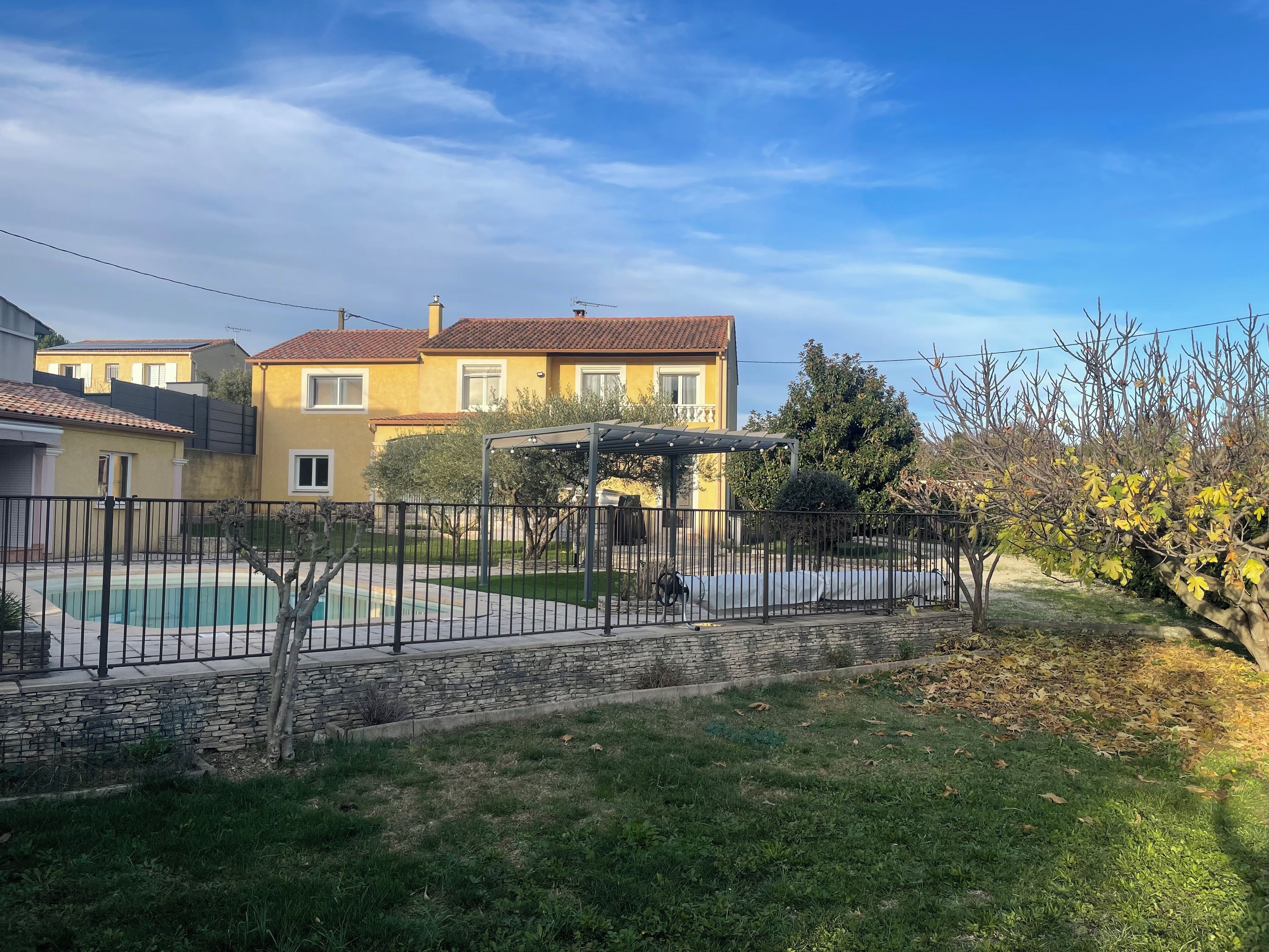 A residential area with a swimming pool, stone wall, and a covered outdoor seating area.