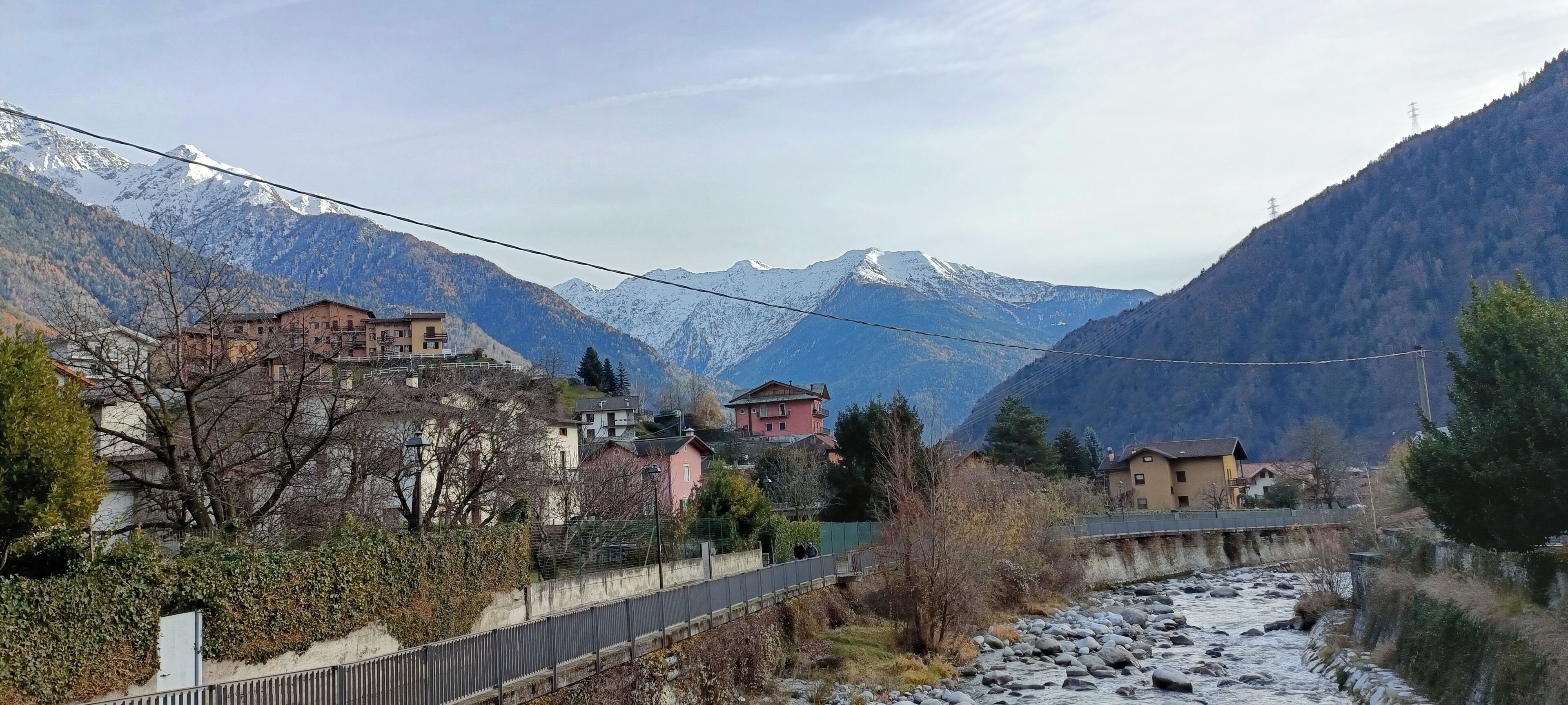 A mountainous village with houses along a river, a bridge, and power lines.