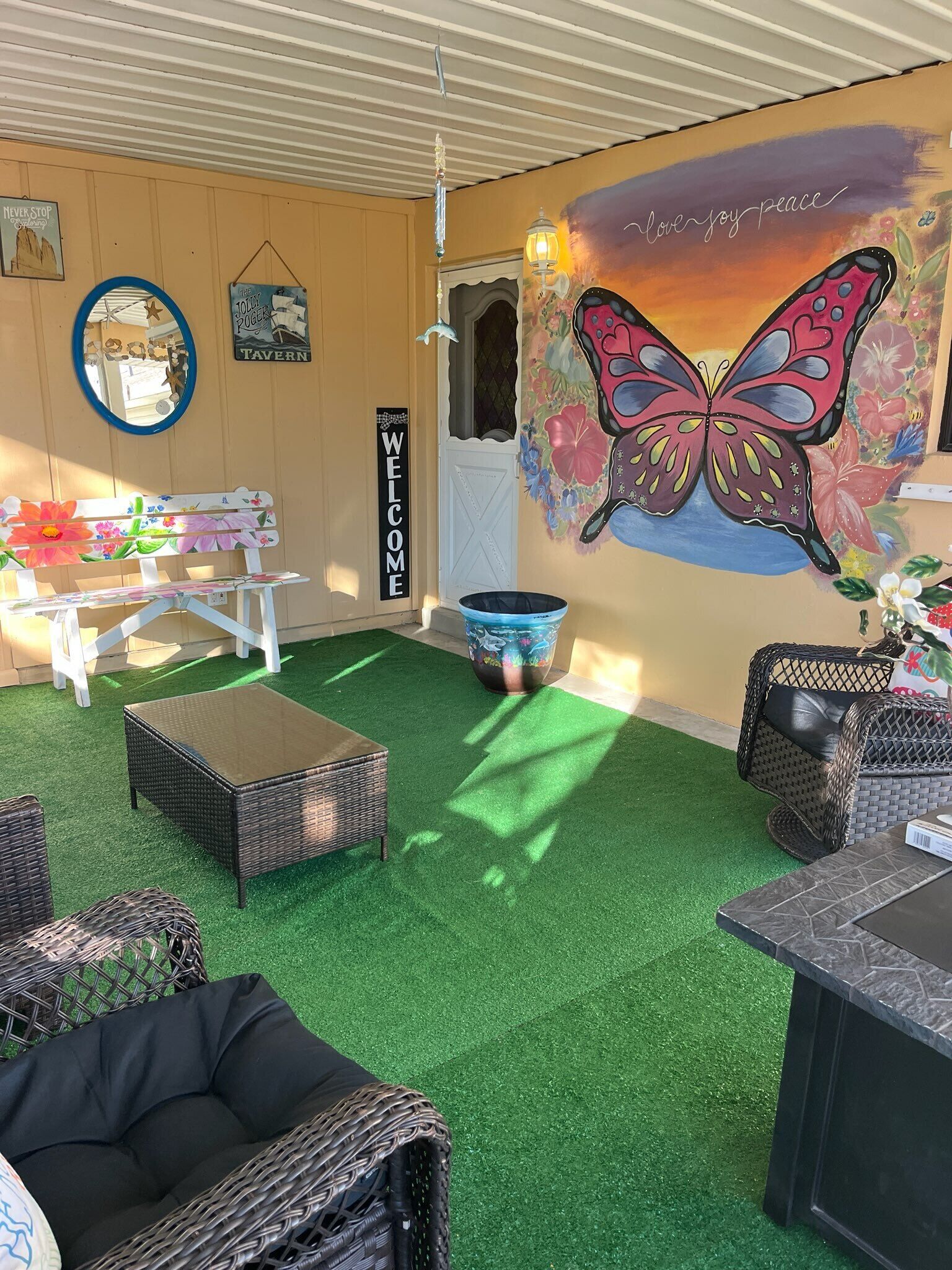 Un rincón interior acogedor con césped artificial, mobiliario de mimbre y un mural de una mariposa.