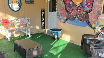 Un rincón interior acogedor con césped artificial, mobiliario de mimbre y un mural de una mariposa.