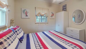 Ein Schlafzimmer mit Bett, Kleiderschrank, Kommode, einem Fenster mit Vorhängen und Wandbildern.