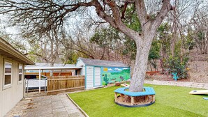 Ein Garten mit Baum, Spielhaus und umzäunter Fläche.